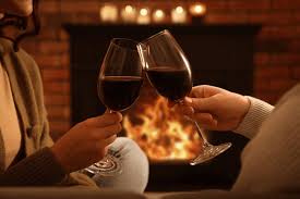 A warm, intimate moment with two people clinking glasses by the fire.