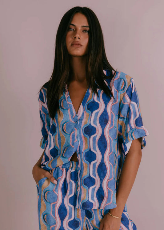 Model wearing Corfu Shirt in Greece Print Blue with boxy fit, short cuffed sleeves, button-through front and scooped hemline