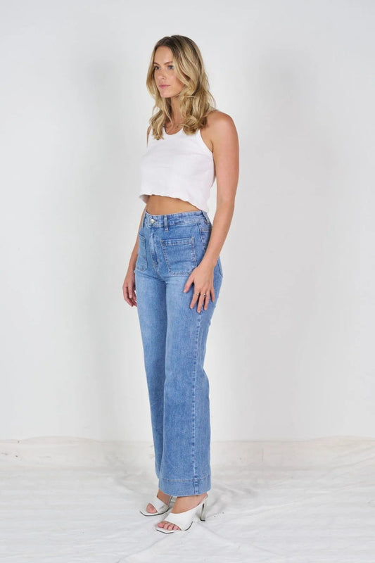 Woman in light blue wide leg jeans with high-rise waist and front patch pockets, styled with a relaxed tank for a casual look.