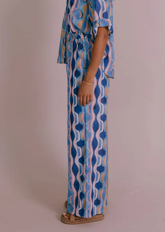 Woman wearing wide-leg blue and white Greece print pants with elastic waist, styled for a relaxed summer look from Vivian The Store
